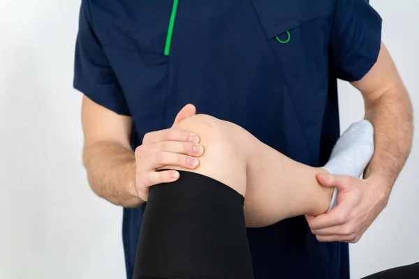 Lékař nebo fyzioterapeut pracující vyšetřuje léčbu poraněné nohy atletického pacienta, Dělat rehabilitační terapie bolest na klinice. — Stock fotografie