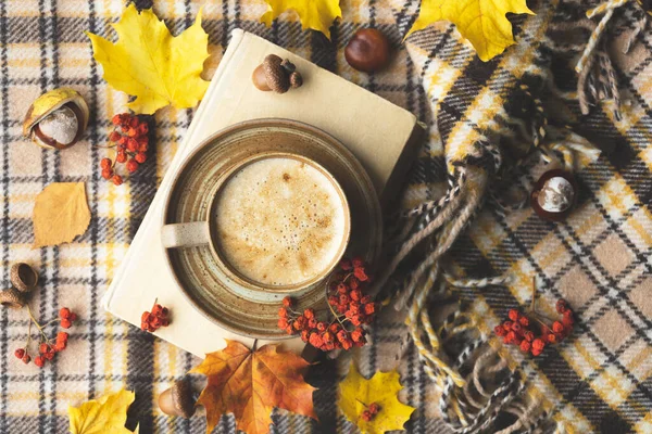 Atmospheric cozy autumn composition. Hot mug of coffee, book, fall leaves, chestnut, ashberry, acorns and cozy brown plaid as background. Sunday loneliness relaxing, hugge mood. Flat lay, top view.