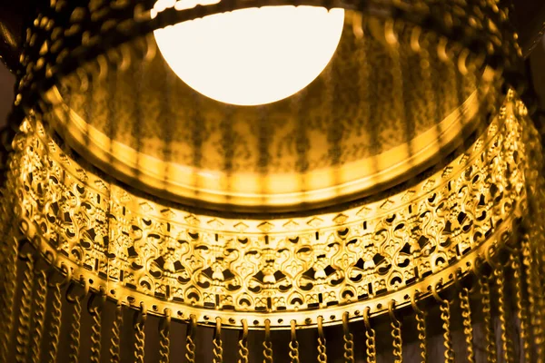 Traditional Oriental lamp. Concept of moody luxury arabic interior in the art deco style. The faint dim light of the golden chandelier with with long chains. Soft focus. Details of lacy metal lamps — стоковое фото