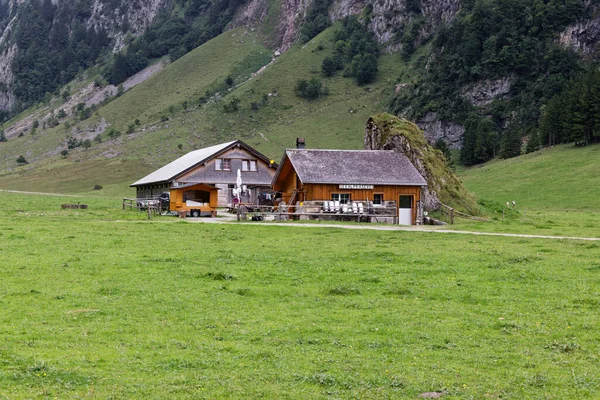 2021年8月19日瑞士 古老风格的高山奶牛 建在石墙旁边 房子前面是空的牛奶罐 德国高山奶牛 在前景广阔的绿色草地上 在带有冷杉林的背景石墙中 — 图库照片