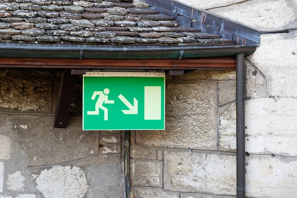 large green emergency exit sign fixed under a tiled roof, castle entrance, safety for all visitors, during the day without people