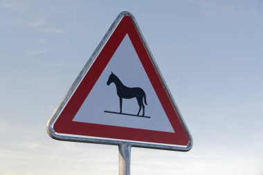 attention horses sign warns of unattended animals on the roadway specifically for horses, in the daytime against a blue cloudless sky