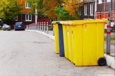 Atıkları ayırmak için farklı renklerdeki atık kapları. Çöp tenekeleri caddedeki çok katlı bir binanın avlusunda.