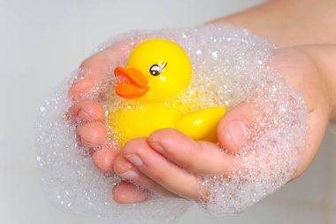 Çocukların ıslak ellerinde sevimli sarı ördek. Çocuk küçük bir oyuncağa özen gösteriyor. Su oyunları. Banyo oyun oynanacak bir yerdir..