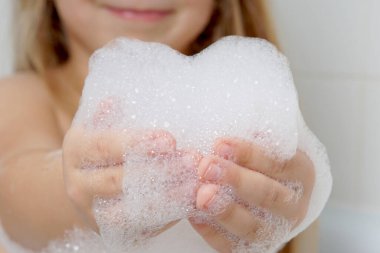 Çocukların ellerinde sabun köpüğünden yapılmış bir kalp. Banyodaki çocuk köpükle oynuyor. Kalp sevginin, özenin, şefkatin sembolüdür. Arkaplanda bir çocuğun bulanık görüntüsü