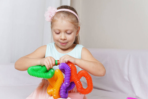 pop tube. anti-stress sensory plastic toy from a tube in the hands of a child. beautiful baby girl playing new modern toy pop tube. trend of 2021. A corrugated tube bent into an interesting metamorphosis shape. Toffee.
