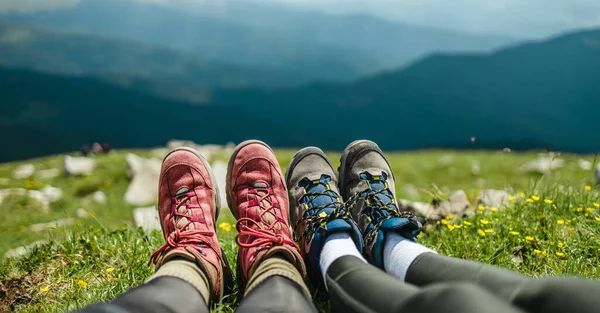 Young couple camping in mountain. Hiker feet in trekking boots relaxing after a long hike on the top of hill on sunny day. Vacation and travel. Amazing Carpathians mountain panorama