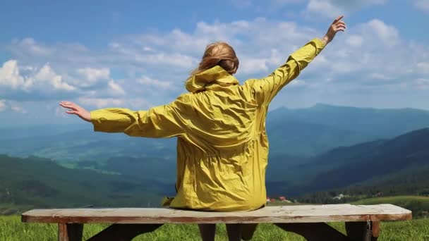 Wanderin hebt die Hände und sitzt an einem sonnigen Sommertag auf einem Felsen. Schöne Berge Landschaft Blick — Stockvideo
