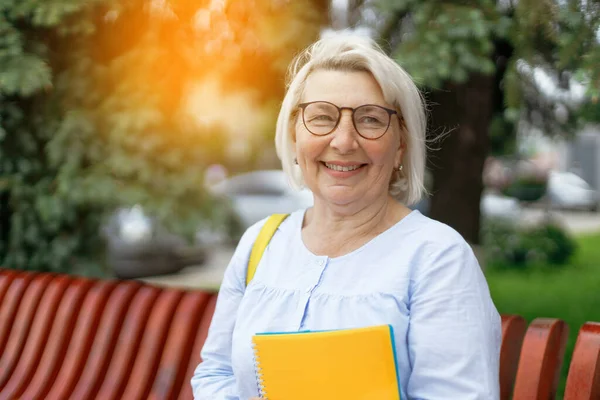 Sorrindo loira professora senhora 40 anos de idade usando óculos de pé segurar notepads olhando câmera ao ar livre — Fotografia de Stock