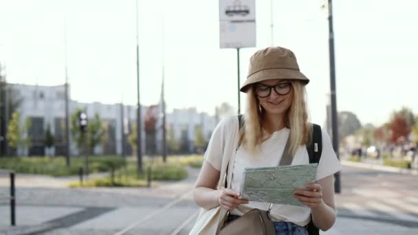 Mladá turistka s batohem hledá správný směr na mapě čeká na veřejnou dopravu na tramvajové zastávce venku. Cestování do Evropy — Stock video