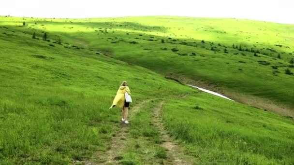 Escursionista solista femminile in giacca gialla brillante in un viaggio tra le montagne di campagna. Colline verdi — Video Stock