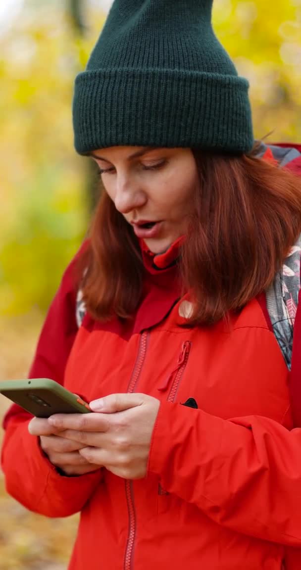 Glad förvånad flicka använder smartphone, utbyta meddelanden, titta på video när du reser eller promenader i parken. Kvinna i varma ljusa kläder på en promenad — Stockvideo