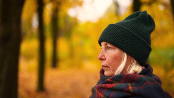 Mujer de cabello rubio adulto con un sombrero verde cálido y con una bufanda camina en un parque de oro de otoño. Humor de otoño, alfombra de hojas amarillas — Vídeo de stock