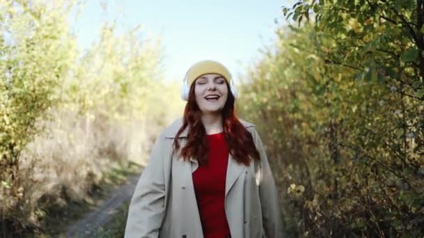 Jovem feliz mulher caucasiana hipster se divertindo, ouvindo música e dançando na rua ao ar livre, parque de outono da cidade. Conceito de tecnologia e felicidade. — Vídeo de Stock