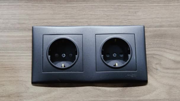 Felame hand inserts the plug into electric socket. Grey plastic power socket and power plug on wood wall — Stock Video