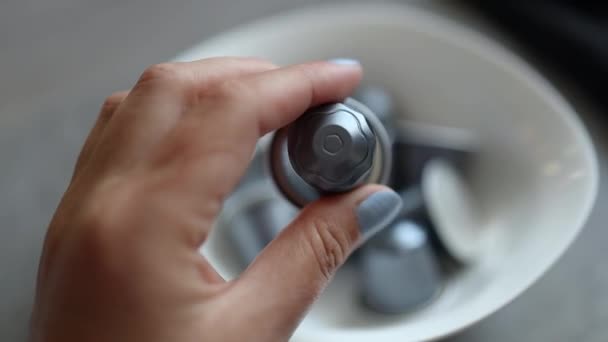Person tar en liten silverkapsel till en automatisk kaffemaskin från en vit tallrik i köket — Stockvideo