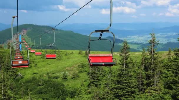 Lanovka s červenými sedadly v horském údolí s dřevěnými domky a chalupami proti zatažené modré obloze. Lesy malebný pohled — Stock video