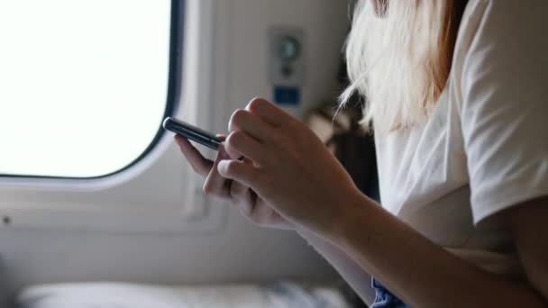 Viaja joven sentada en un tren con un smartphone en las manos. — Vídeos de Stock