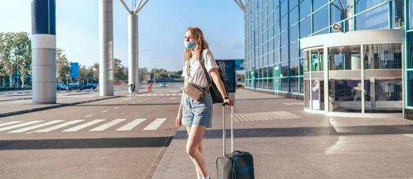 Woman tourist with backpack standing near the airport with luggage while traveling in the mountains. Young caucasian girl in a protective medical mask — Stock Photo, Image