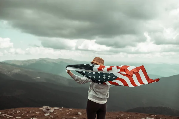 Dziewczyna macha amerykańską flagą na szczycie góry na tle nieba. Dzień Niepodległości — Zdjęcie stockowe