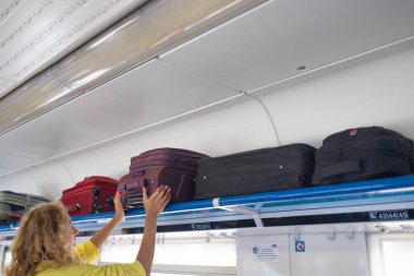 Kadın elleri el bagajlarını çıkarır. Genç bayan bagajı trendeki rafa koyuyor.