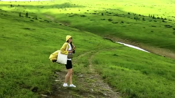 Perempuan pejalan kaki dengan jaket kuning terang dalam perjalanan di pegunungan pedesaan. Bukit gelombang hijau — Stok Video
