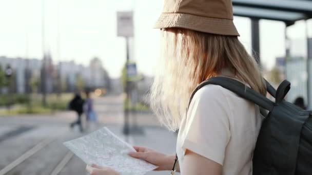 Giovane turista con zaino cerca la giusta direzione sulla mappa in attesa dei mezzi pubblici alla stazione del tram all'aperto. Viaggio in Europa — Video Stock