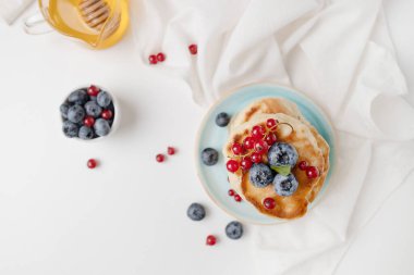 Kahvaltı için arka planda beyaz bir masada taze yaban mersini, ahududu ve bal pekmezli leziz gözlemeler, fotokopi odası. Üst manzara, düz uzanma