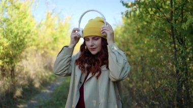 Genç mutlu hippi bayan gezgin sonbahar parkında kablosuz kulaklık takıyor. Rüzgarda kıvırcık kıvırcık renkli saçlar