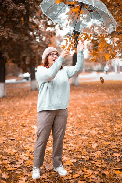 Lány szórakozás közben átlátszó esernyő alatt őszi városi parkban — Stock Fotó