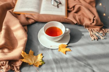 Sıcak örülmüş bej eşarp, bir fincan sıcak bitkisel yeşil çay ve rahat yatakta açık bir kitap. Hygge konsepti.