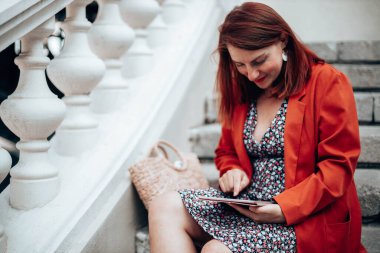 Şık giyinmiş, gülümseyen bir iş kadınının portresi sokakta otururken modern tablet cihazını kullanıyor.