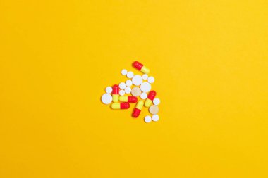 Sarı arka planda çeşitli ilaç hapları, haplar ve kapsüller, düz yatış