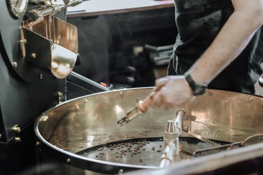 Adam kahve çekirdeklerini kızartma makinesine döküyor.