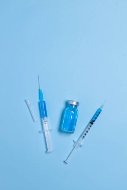 Açık mavi arka planda iğneler ve şişe ile tek kullanımlık şırıngalar, yakın plan, aşı ve bağışıklık konsepti