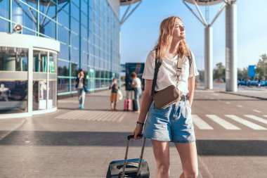 Seyahat eden kadın turist sırt çantası ve el çantasıyla uluslararası havaalanı terminalinin yanında uçağa binmek için bekliyor. Etkin yaşam tarzı kavramı