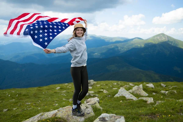 Kobieta trzymająca flagę USA na szczycie góry i ciesząca się widokiem jesiennych wzgórz skalnych. Obchody Dnia Niepodległości Ameryki — Zdjęcie stockowe