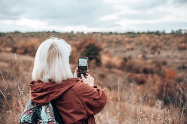 Altın sonbahar parkında akıllı telefonla fotoğraf çeken kadın turist elleri.