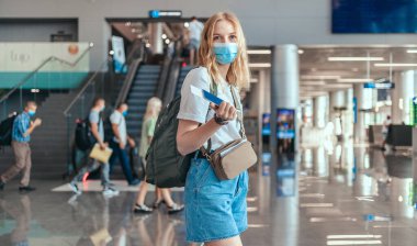 Bavullu sarışın kadın turist pasaportu havaalanı terminalinde yolculuk için bekliyor. Covid-19 salgınından sonra seyahat