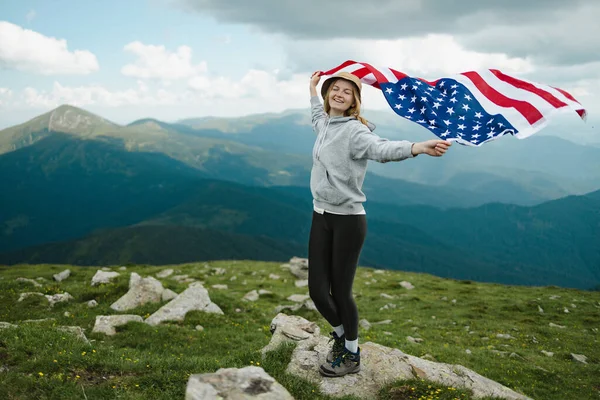 Kobieta trzymająca flagę USA na szczycie góry i ciesząca się widokiem jesiennych wzgórz skalnych. Obchody Dnia Niepodległości Ameryki — Zdjęcie stockowe