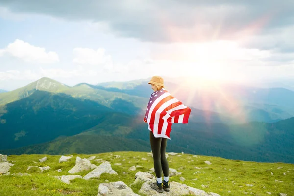Kobieta macha amerykańską flagą na szczycie góry na tle nieba, świętując dzień niepodległości — Zdjęcie stockowe