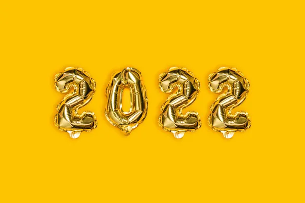 Happy new year 2022 gold foil holiday balloons on yellow background. Flat lay, top view.