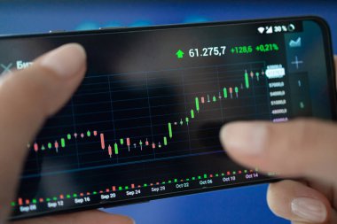Ticari yatırımcı akıllı telefondan tartışıyor ve analiz ediyor. Satmak, satın almak ve kâr payı istatistiklerini analiz etmek için mali başvuru