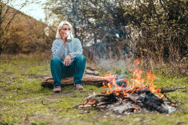 Gezgin kadın ormanda kamp yapıyor ve yorucu bir günün ardından kamp ateşinin yanında dinleniyor. Yürüyüş, macera ve mevsimlik tatil kavramı. — Stok fotoğraf