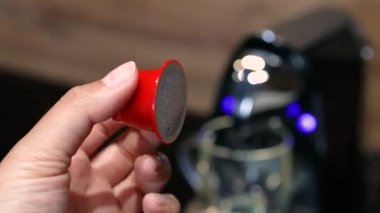 Kadın eli, mutfaktaki beyaz tabaktan otomatik kahve makinesi için küçük kırmızı bir kapsül alır.