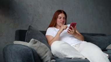 Evdeki oturma odasında cep telefonu kullanan güzel beyaz bir kadın. Sosyal medyayı izliyordum. Teknoloji iletişim konsepti