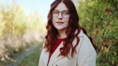 Çekici genç bir kızın portresi yürüyor ve sonbahar parkının dışındaki ormanda Coronavirus yüzünden karantinadan sonra dinlenirken kameraya gülümsüyor..