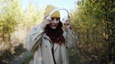 Beyaz neşe saçan, gülümseyen güzel bir genç kadın müzik dinliyor ve şehir sonbahar parkında dans ediyor. Şık giyinmiş kıvırcık saçlı bir kadın müzikten hoşlanıyor.