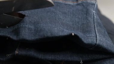 Profesyonel terzi tasarımcı atölyede dikiş masasında mavi kot kumaşı makasla kesiyor..