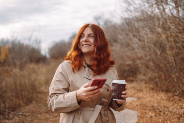 Akıllı telefon kullanan ve kahve içen neşeli bir kadın.